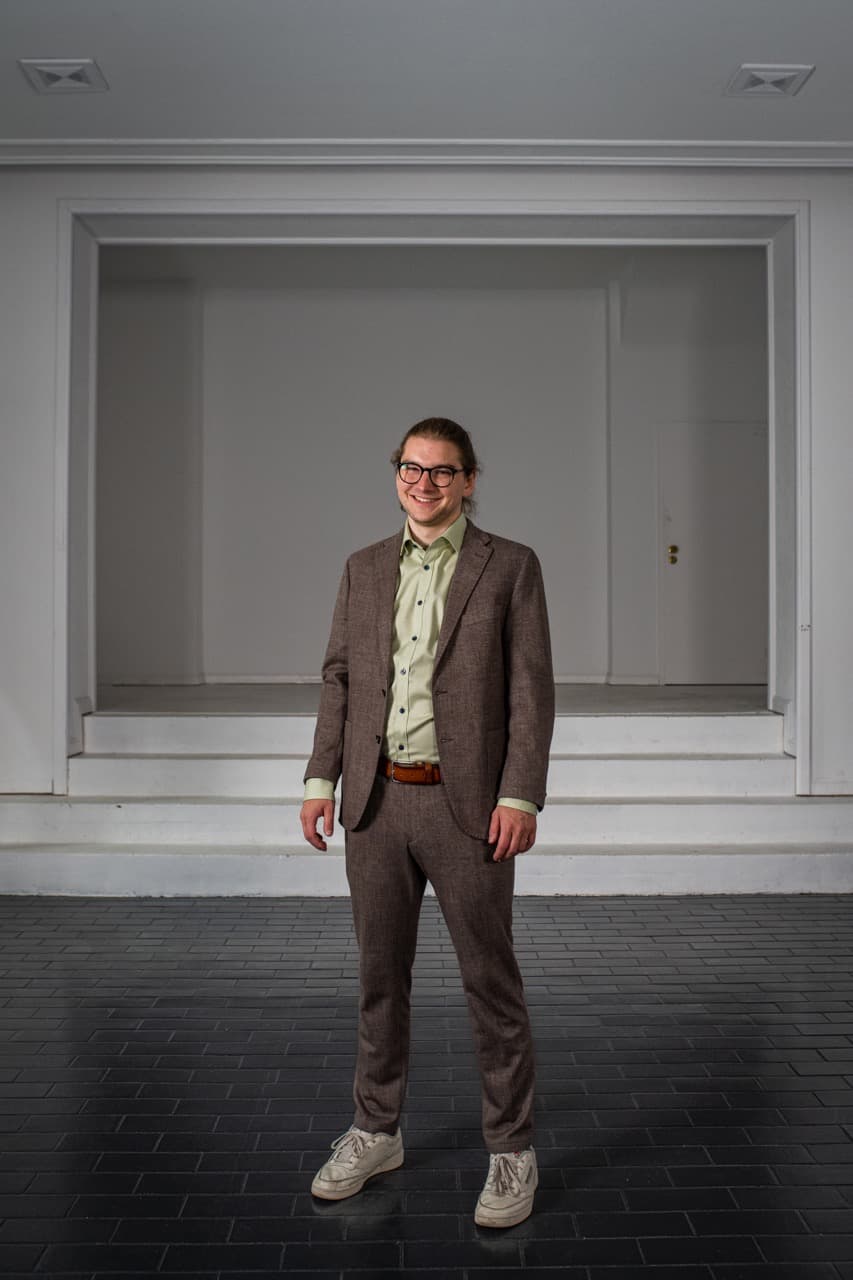Oliver Wycisk, stehend im Anzug vor einer weißen Wand